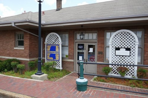 A brick building with a sign reading "OPEN" and decorative latticework, surrounded by greenery and a sidewalk.