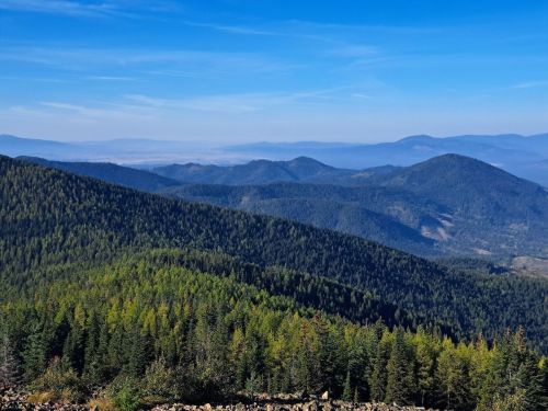 A panoramic view of lush green mountains under a clear blue sky, with distant hills fading into the horizon.