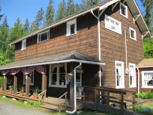 A two-story wooden building with a porch, labeled "Museum," surrounded by trees and potted plants.