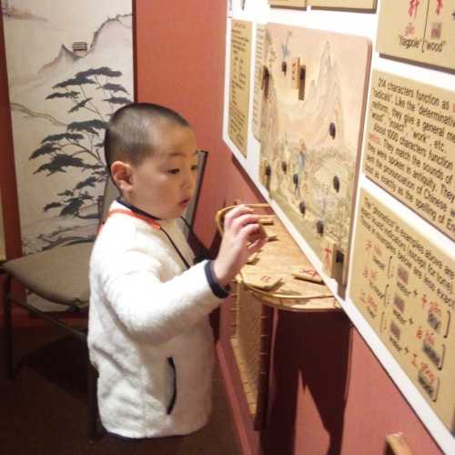 A young child interacts with a wooden educational display in a room with Asian-themed decor.