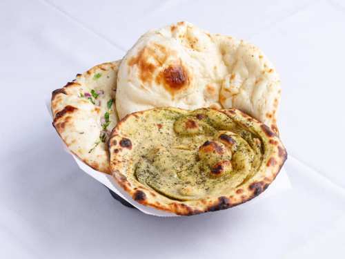 A basket of assorted naan breads, including plain, garlic, and herb varieties, on a white tablecloth.