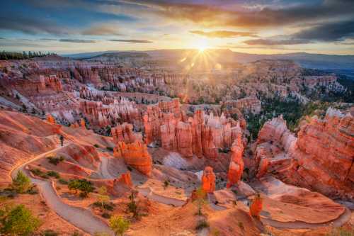 Sunrise over Bryce Canyon, highlighting orange rock formations and a winding path through the stunning landscape.