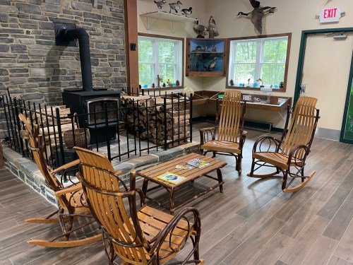 Cozy indoor space with rocking chairs, a wood stove, and a stack of firewood, surrounded by nature-themed decor.