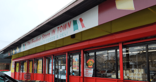 A colorful storefront with a red facade, featuring signs for a grocery and deli called "The Friendliest Store in Town."