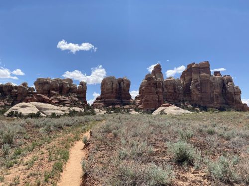 A scenic view of towering rock formations against a blue sky, with a dirt path winding through the surrounding grassland.
