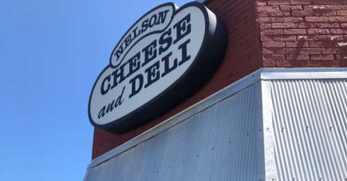 Sign for "Nelson Cheese and Deli" on a brick building with a clear blue sky in the background.