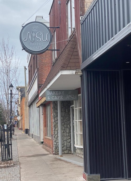 A street view of a bakery and café with a sign reading "NISU Bakery & Café" on a cloudy day.