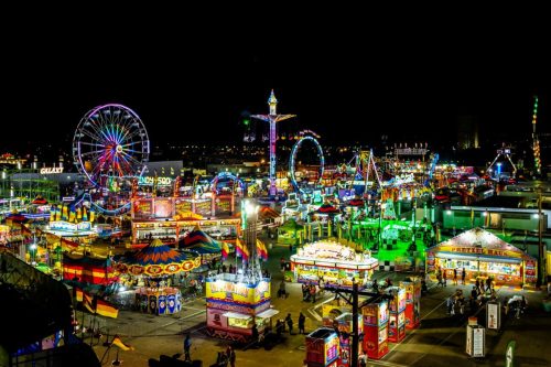 A vibrant night scene of a carnival with colorful lights, rides, and food stalls bustling with activity.