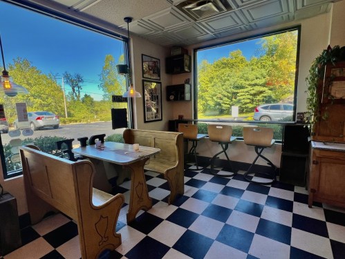 Cozy diner interior with checkered floor, wooden seating, and large windows showcasing a sunny outdoor view.