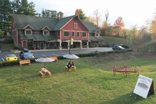 A red building with a green roof houses Noble Pie, surrounded by outdoor seating and trees in autumn colors.