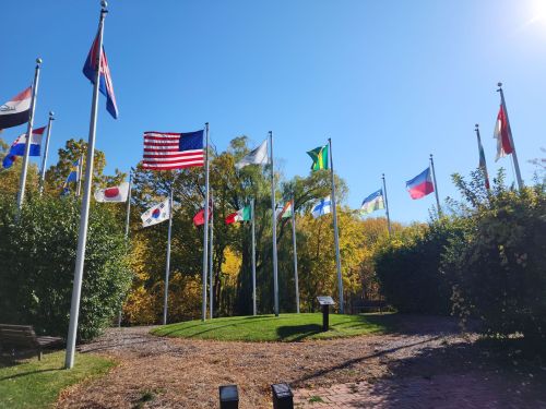 A circular area with various national flags on poles, surrounded by greenery and trees under a clear blue sky.