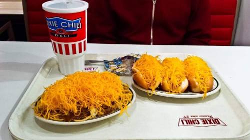 A tray with two plates of chili cheese dogs topped with shredded cheese and a large drink in a cup.