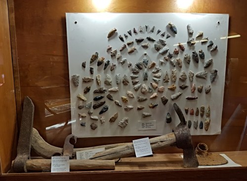 Display case featuring various stone tools and artifacts, including arrowheads and axes, arranged on a board.