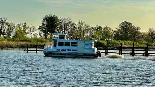 A boat labeled "North Carolina Public Schools" navigates a calm waterway surrounded by greenery.