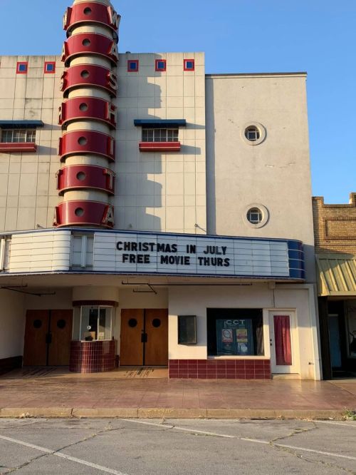 A vintage movie theater with a marquee reading "Christmas in July" and "Free Movie Thurs" on a sunny day.