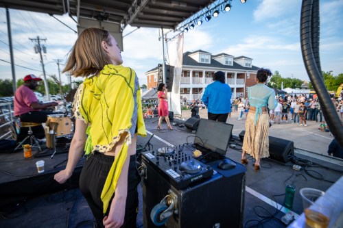 A lively outdoor concert scene with performers on stage and an audience enjoying the music.
