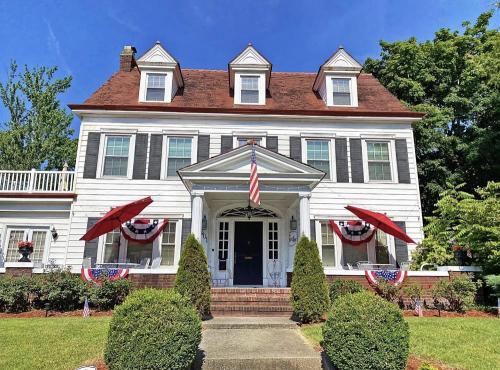 A charming white house with a red roof, featuring American flags and decorative bunting on a sunny day.