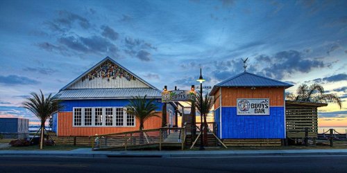 Colorful beach bar at sunset, featuring blue and orange walls, palm trees, and a welcoming entrance.