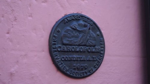 A bronze plaque mounted on a pink wall, commemorating an award from 1968 by the Preservation Society of Charleston.