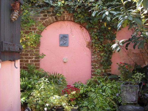 A serene garden with pink walls, lush greenery, and a decorative archway, creating a peaceful outdoor space.