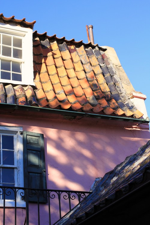 A colorful rooftop with terracotta tiles and a pink wall, featuring a green window and a clear blue sky.
