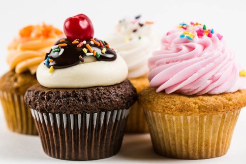 A variety of colorful cupcakes with different frosting and toppings, including sprinkles and a cherry on top.