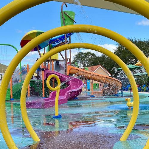 Colorful water play area with slides and splash features, framed by bright yellow arches under a clear blue sky.