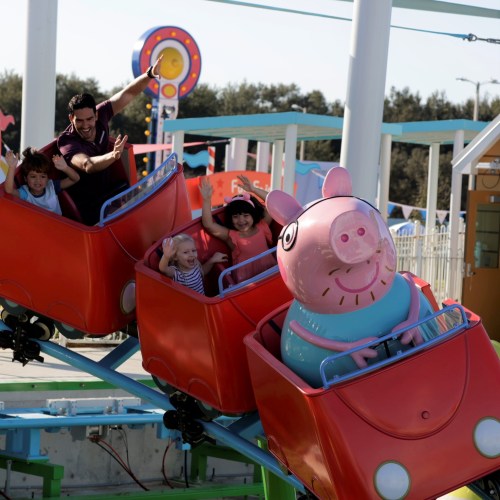 A group of children and an adult enjoy a colorful amusement park ride featuring a character resembling a pig.