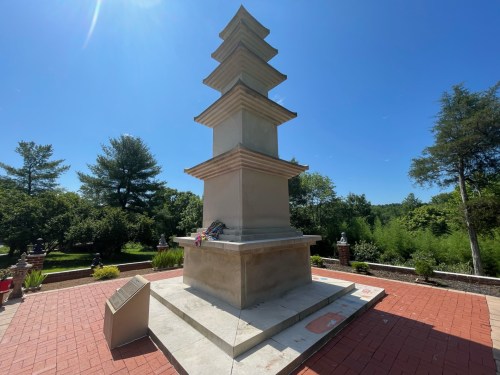 A tall, multi-tiered stone monument surrounded by greenery under a clear blue sky.