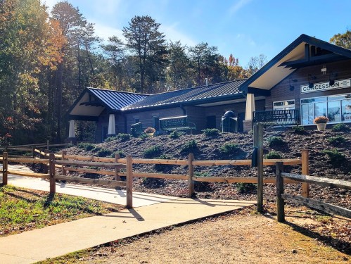 A modern concession building surrounded by trees and a pathway, with a clear blue sky above.