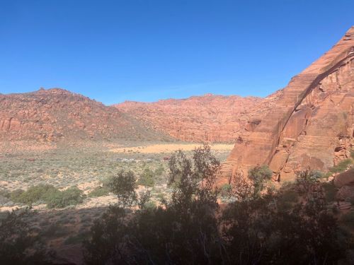 A scenic view of red rock formations and a green valley under a clear blue sky.