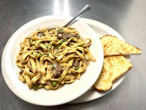 A bowl of fettuccine pasta with beef and peas, served with two slices of toasted bread on the side.