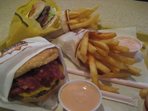 A tray with a burger, fries, and dipping sauces, featuring a wrapped sandwich and a side of crispy French fries.