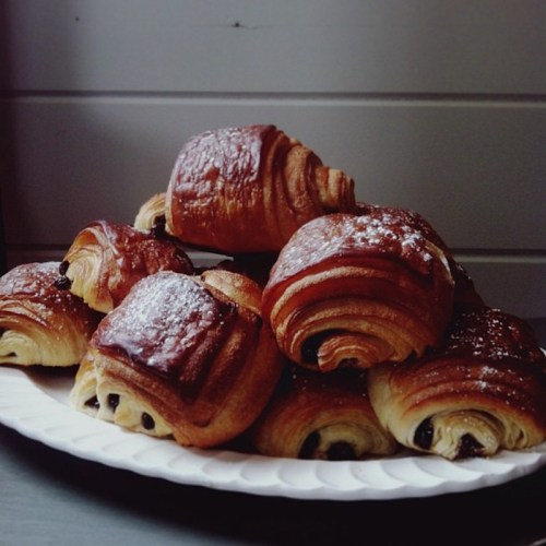 A plate of freshly baked croissants, some with chocolate filling, dusted with powdered sugar.