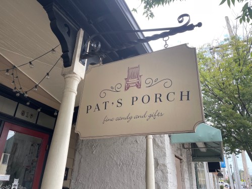Sign for "Pat's Porch" featuring fine candy and gifts, hanging from a building with a porch view.
