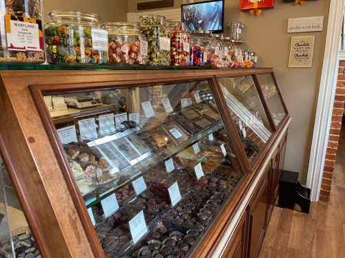 A display case filled with various chocolates and candies, with jars of sweets on top and a cozy shop atmosphere.