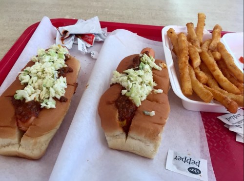 Two chili hot dogs topped with coleslaw on a tray, accompanied by a side of crinkle-cut fries.