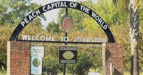 Sign archway reading "Peach Capital of the World" and "Welcome to Johnston," surrounded by greenery.