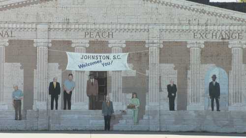 Mural depicting a welcoming scene in Johnston, SC, featuring figures in front of a historic building with a banner.