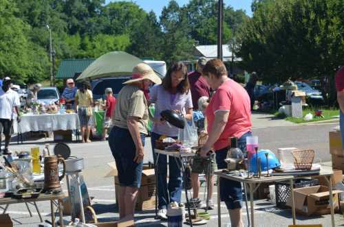 Three women browse items at a bustling outdoor flea market, surrounded by tables filled with various goods.