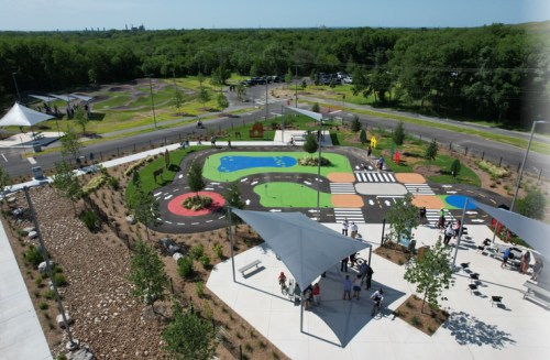 Aerial view of a colorful playground with pathways, water features, and shaded seating areas surrounded by greenery.