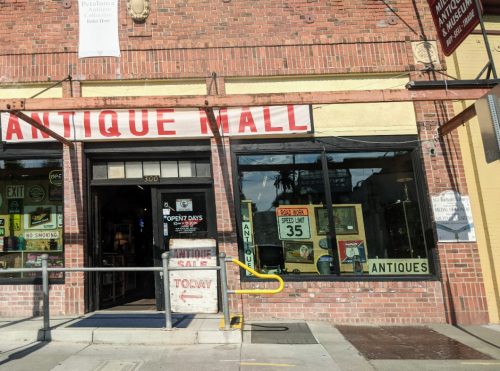 Exterior of an antique mall with a large sign reading "Antique Mall" and a display of antiques in the windows.