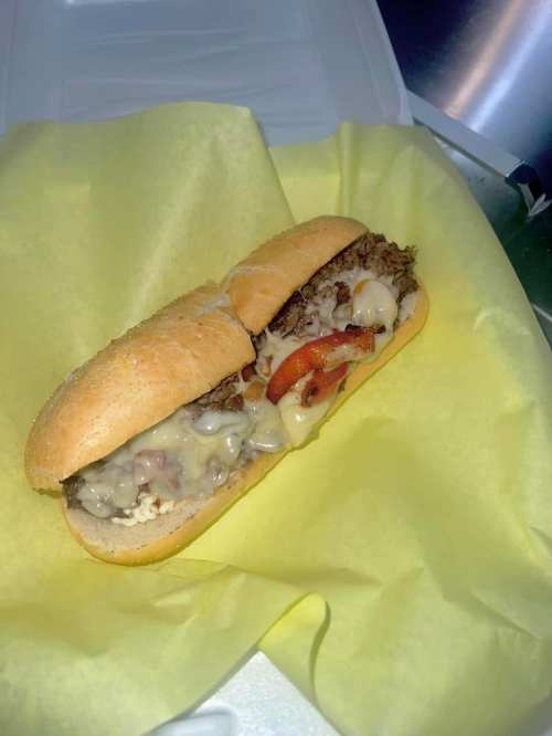 A sandwich with melted cheese, sliced beef, and peppers, served in a soft hoagie roll on yellow paper.