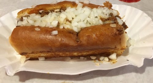 A hot dog in a bun topped with chopped onions, served on a white paper plate.