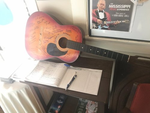 An autographed guitar rests on a table next to a notebook and pen, with a poster in the background.