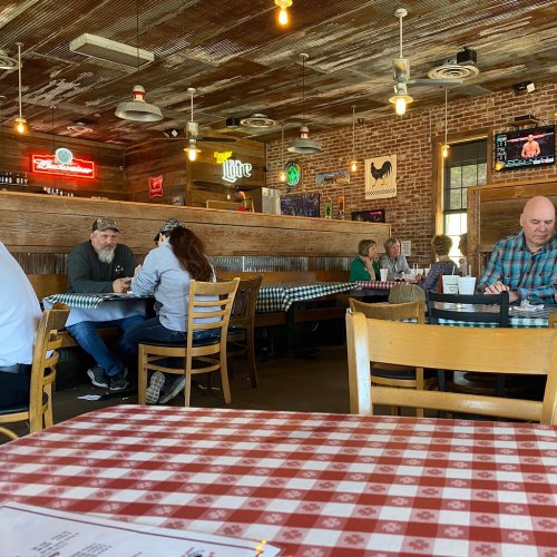 A rustic restaurant interior with wooden booths, checkered tablecloths, and patrons dining and chatting.