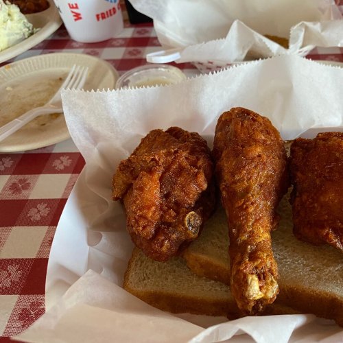 Three pieces of fried chicken on white bread, served on a checkered tablecloth with a side of dipping sauce.