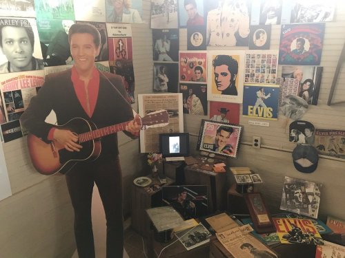 A life-size cutout of Elvis Presley stands among vintage records, posters, and memorabilia in a nostalgic display.