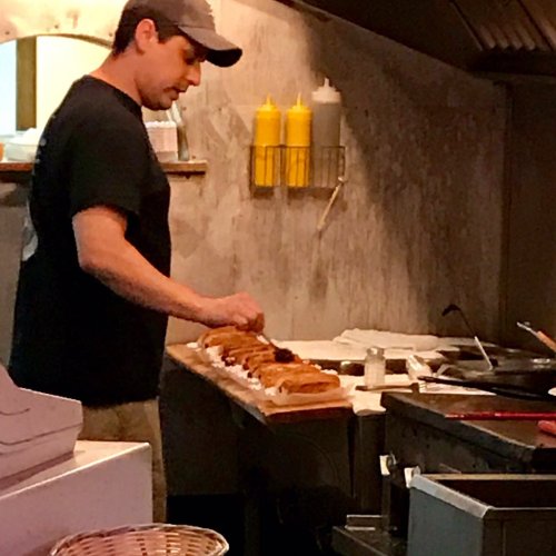 A chef prepares food in a kitchen, arranging dishes on a wooden board with condiments in the background.