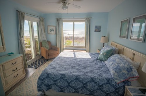 Cozy beachside bedroom with a blue color scheme, large window, and a view of the ocean.